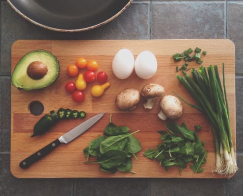 A cutting board and knife are laid out with healthy ingredients and a fry pan.