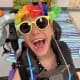 Young adult with cerebral palsy, wearing a colorful hat, yellow sunglasses, smiling joyfully at the camera.