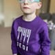 A serious young boy with cerebral palsy wearing blue glasses and a purple sweater.