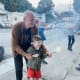 A smiling man helps a young boy with cerebral palsy to hold a sparkler. The boy is wearing glasses and ankle foot orthotics.