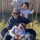 A child with cerebral palsy swings in a backyard basket swing together with a smiling woman and two other children.