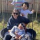 A child with cerebral palsy swings in a backyard basket swing together with a smiling woman and two other children.