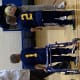 A young boy with cerebral palsy, using a walker, stands in a school gymnasium looking at an adult holding a basketball.