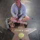 A smiling woman with cerebral palsy, wearing glasses, sits cross-legged in front of a Veronica Lake Hollywood star.