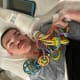 A young man with cerebral palsy lies in bed while listening to an iPad and holding a colorful chain of sensory toys.