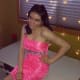 A smiling young woman with cerebral palsy sits with her hand on her hip while wearing a pink dress.