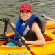 Adult female with cerebral palsy smiles in a kayak as she paddles.