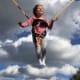 A little girl with CP laughs as she soars on a bungee harness against a backdrop of the blue sky and fluffy grey-and-white clouds.