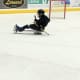 A young boy with cerebral palsy, wearing a black helmet and winter clothes, plays adaptive sled hockey in an indoor ice arena.