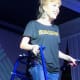 A smiling woman with cerebral palsy, wearing a dark grey t-shirt and jeans, stands with a royal blue walker on a stage.