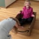 A laughing girl with cerebral palsy is towed across the floor by another child while sitting in a cardboard box.