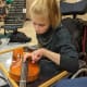 A child with cerebral palsy is sitting in her wheelchair in a brightly-lit auditorium while holding a violin.