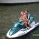 A smiling woman with CP sits in front of a man as they ride a blue-and-white jet ski together.
