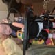 A baby with cerebral palsy uses a standing frame with a desk to play with a yellow toy car while an adult supports her head.