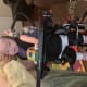 A baby with cerebral palsy uses a standing frame with a desk to play with a yellow toy car while an adult supports her head.