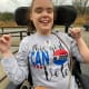 A woman with cerebral palsy smiles broadly from her wheelchair while wearing a light grey ‘This girl can vote’ sweater.