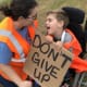 A young boy with CP in a wheelchair and a woman smile at each other. The boy is holding a sign that reads ‘Don’t Give Up’.