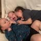 Three laughing toddler triplets, wearing navy-blue leopard-print pajamas, cuddle together on a white blanket.