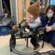 A toddler with cerebral palsy, helped by a therapist, uses a gait trainer to walk in a hospital clinic.