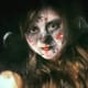 A slightly smiling girl with cerebral palsy wearing white, black, and red face paint.