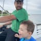 A laughing young boy with CP, wearing a blue life jacket, sits next to a man who is steering the boat they are sailing on.