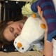 A girl with cerebral palsy, wearing an arm cast, sleeps in her wheelchair while cradling a grey-and-white stuffed toy penguin.
