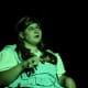 A young woman with cerebral palsy, cast in a green light and wearing a ‘Dorothy’ costume from ‘The Wizard of Oz’.