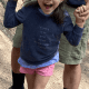A smiling little girl with cerebral palsy walks up a trail while supported by an adult holding her hands.