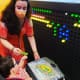A woman helps a young boy with cerebral palsy, who is seated in a wheelchair, to play with a colorful light board.