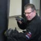 A man with CP, wearing glasses, a black uniform, and padded gloves, punches a black boxing bag from his wheelchair.