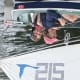 A smiling adult with cerebral palsy and another adult are both seated as they enjoy sailing in a blue-and-white sailboat.