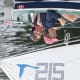 A smiling adult with cerebral palsy and another adult are both seated as they enjoy sailing in a blue-and-white sailboat.