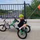 A man with cerebral palsy smiles towards the camera while riding his green recumbent tricycle across a highway overpass.