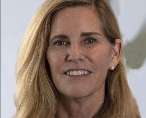 Laurie Glader, MD, with side swept shoulder length blonde hair smiles in a lavender shirt.