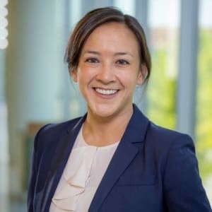 Dr. Sarmiento smiles broadly with her brown hair pulled back, in a navy blazer and light colored swoop neck blouse.