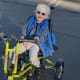 A boy with cerebral palsy with white hair and sunglasses smiles riding his trike.