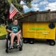A young man in a wheelchair sits next to a neon sign advertisting his lemonade