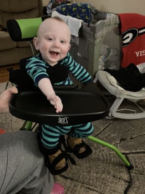 A boy with cerebral palsy in his stander wearing green and blue striped pajamas.