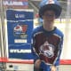 A young man standing in an ice hockey jersey and hat at an ice rink.