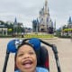 A young boy in a blue shirt smiles in his stroller at Disneyland