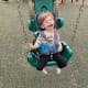 A young boy smiles gleefully strapped into a child swing.