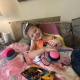 A young girl with cerebral palsy smiles lying back on a couch with a set of adaptive toys.