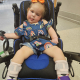 A young girl with cerebral palsy with an orange bow in her hair sticks her tongue out.