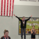 A young girl with a genetic cerebral palsy stands on the #1 podium for gymnastics with her arms outstretched