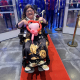 A woman in a wheelchair smiling in her dress and a tiara and holding a pink heart shaped balloon