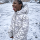 A child with cerebral palsy in a white winter jacket catches snowflakes on his tongue