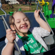 A young girl with cerebral palsy smiles with her eyes closed in a stroller in an outdoor park.