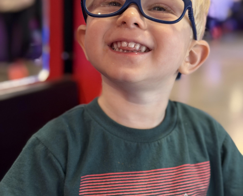 A young boy with blonde hair and blue glasses has a genetic cerebral palsy