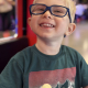 A young boy with blonde hair and blue glasses has a genetic cerebral palsy