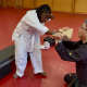 A young girl with cerebral palsy stands in a while gi chopping a board in half